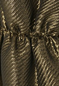 Tessuto in bronzo metallico con una superficie texturizzata e ondulata. La plissettatura è visibile, creando pieghe in tutto il materiale.