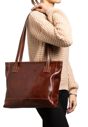 Persona che indossa un maglione beige lavorato a maglia, con una grande borsa tote in pelle marrone sulla spalla, su uno sfondo bianco.