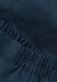 Mörkblått tyg med en slät textur och samlad volangdetalj. Materialet verkar lättviktigt och har en lätt glans.