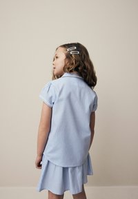 Blauw-wit geruite jurk met een kraag, korte puffmouwen en een uitlopende rok. Inclusief haarspeldjes in het haar van het kind.
