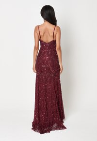 Burgundin korkea paljettimekko, jossa on monimutkaisia helmikuviota, hienot spagettiolkaimet ja istuva yläosa, joka virtaa laajahelmaiseen hameeseen.