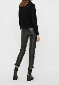 Pull en maille noire associé à un pantalon en cuir noir ajusté, présentant une texture lisse et un léger éclat ; bottines à talons carrés.