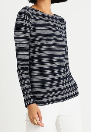 Haut de couleur marine à manches longues avec des rayures blanches horizontales, col rond, texture douce et coupe décontractée, associé à un pantalon blanc.