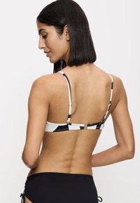 Top bikini con un motivo geometrico in bianco e nero, spalline regolabili e una chiusura dorata sul retro. Tessuto liscio, design minimalista.