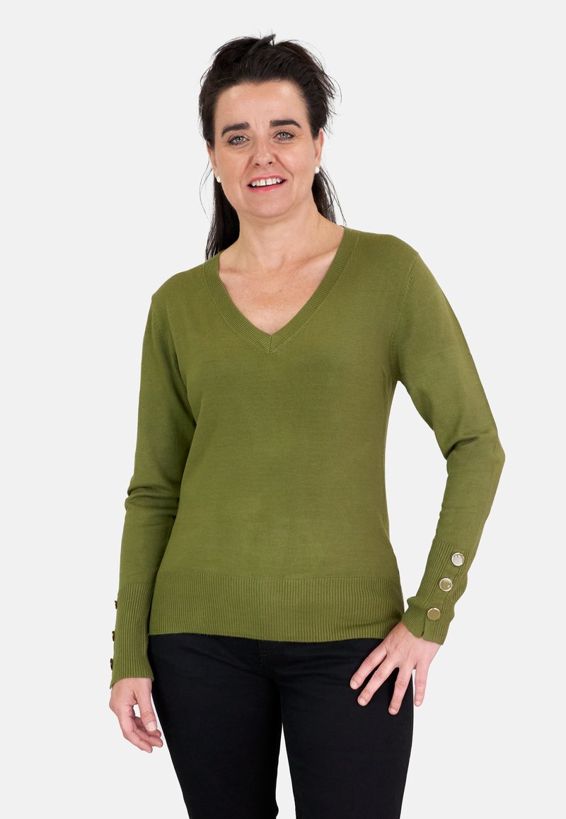 Suéter verde oliva de punto con escote en V, dobladillo acanalado y tres botones decorativos en cada puño. Combinado con pantalones negros.