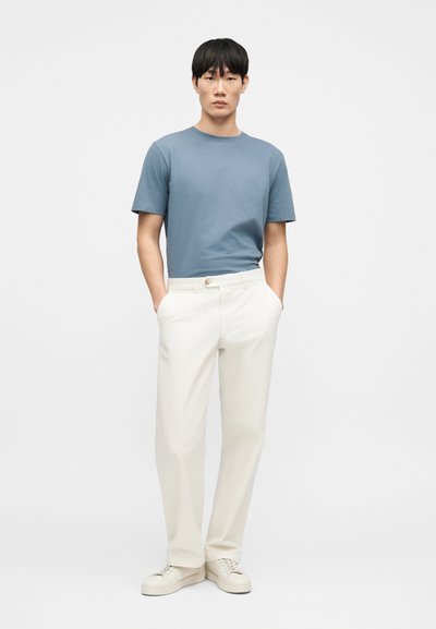 Tenue pour homme composée d'un t-shirt en coton bleu et d'un pantalon blanc. Le t-shirt a un col rond ; le pantalon est ample avec un détail de bouton.