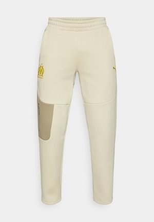 Cremefarbene Jogginghose mit gelbem Logo und Akzenten. Verfügt über einen elastischen Bund, seitliche Tasche mit Reißverschluss und kontrastfarbene Aufnäher.