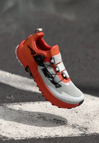 Chaussure de course avec un schéma de couleurs gris et orange, tige en mesh, système de fermeture Boa et design de semelle extérieure robuste pour une meilleure traction.