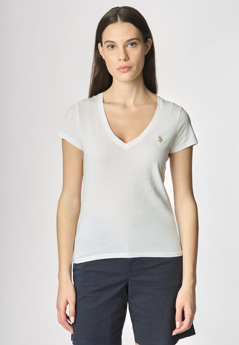 T-shirt bianca in cotone con scollatura a V e maniche corte, presenta un piccolo logo ricamato sul petto. Abbinata a pantaloni corti scuri.