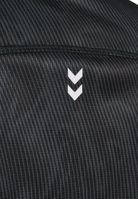 Zbliżenie na czarną prążkowaną tkaninę z dwoma białymi, skierowanymi w dół wzorami w kształcie szewronu i poziomym przeszyciem nad nimi.