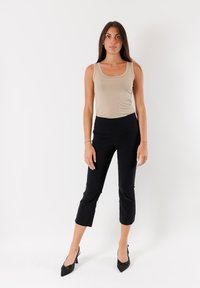 Top in beige, pantaloni neri corti, e tacchi a punta neri. Texture lisce, design aderente, aspetto minimalista, senza motivi o accenti.