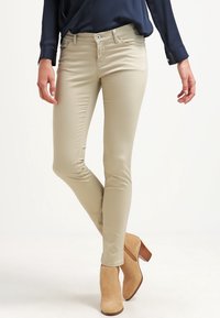 Beige smala jeans med en slät yta, lågt midjeparti, subtila sömmar och framfickor, ihop med ljusbruna ankelboots.