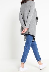 Harmaa, ribbineulottu yläosan kokoinen neulepaita, jossa on pitkät hihat ja takalta etuosaa pidempi helma, yhdistetty sinisiin farkkuihin ja valkoisiin tennareihin.