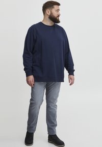 Felpa a maniche lunghe blu navy con collo rotondo, abbinata a jeans grigi chiari e stivali alla caviglia neri. Il tessuto sembra morbido e confortevole.