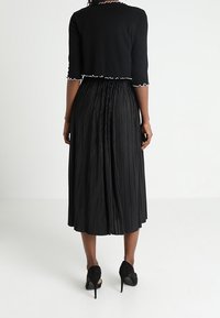 Svart plisserad kjol som sträcker sig till mitten av vadbenet, tillsammans med en kort svart topp med vågiga kanter. Bärs med svarta högklackade skor.