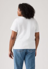 Baltas kokvilnas T-krekls ar īsām piedurknēm un brīvu piegriezumu, apaļu kakla izgriezumu. Kopā ar zilām džinsu biksēm ar aizmugurējām kabatām.