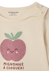 Cremfarbener Baumwollshirt mit einem illustrierten lächelnden lila Apfel und grünen Blättern, versehen mit dem Text "MIGNONNE À CROQUER!" in Braun.