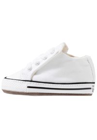 Vit tygskor med gummitåhätta, svarta ränder på sulan och flera skosnöreshål. Insidan har mjukt foder.