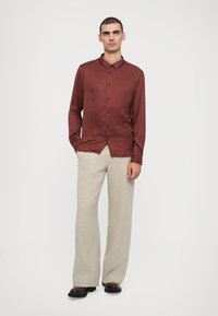 Red patterned shirt with buttons, long sleeves, and a collar paired with beige wide-leg trousers and black shoes on a neutral background.