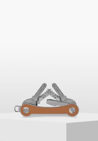 Outil multifonction avec un corps en métal argenté mat, équipé de plusieurs outils et d'une poignée de couleur cuivre. Le design comprend un accent circulaire sur la poignée.