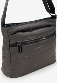 Bolso cruzado gris hecho de tela suave con un patrón acolchado, cierre superior con cremallera y correa ajustable. Presenta un bolsillo frontal con cremallera.