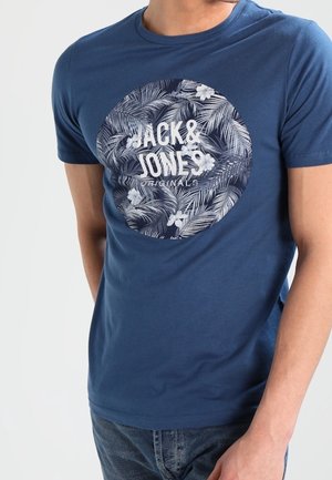 Hombre con camiseta azul marino con un diseño floral circular y el texto "JACK & JONES ORIGINALS" en el pecho.