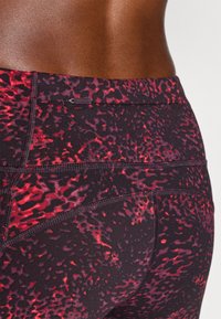 Høyt midjete atletiske leggings i sort og rødt abstrakt mønster. Har flate sømmer og et lite logomerke nær midjen.