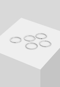 Penkių sidabrinių žiedų rinkinys, pasižymintis įvairiais raštais: lygus, tekstūruotas, sukurtas spiralės forma ir facetuotas. Pagaminti iš metalo, demonstruojant minimalistinį stilių.