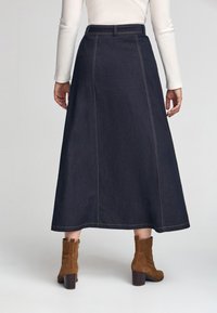 Mörkdenim midi-kjol med synliga sömmar, hög midja och sidofickor. Bärs med bruna mockakängor. Slät yta.