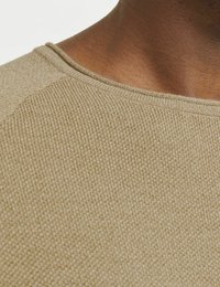 Beżowy sweter dziany z teksturowanej tkaniny, okrągłym dekoltem i delikatnym prążkowaniem na ramionach. Zbliżenie podkreśla detale materiału.