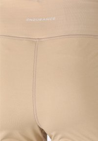 Leggings de sport beiges avec une texture lisse, présentant un logo visible "ENDURANCE" à la taille et des coutures à plat pour plus de confort.