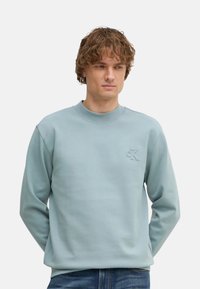 Sudadera azul clara hecha de tela suave, con cuello redondo y logotipo "CK" en relieve en el pecho. Mangas largas y corte relajado.