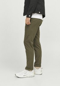 Pantaloni chino din bumbac de culoare verde măslin, cu un croi tapered, cu tivuri răsucite și buzunare laterale, asortați cu adidași albi.