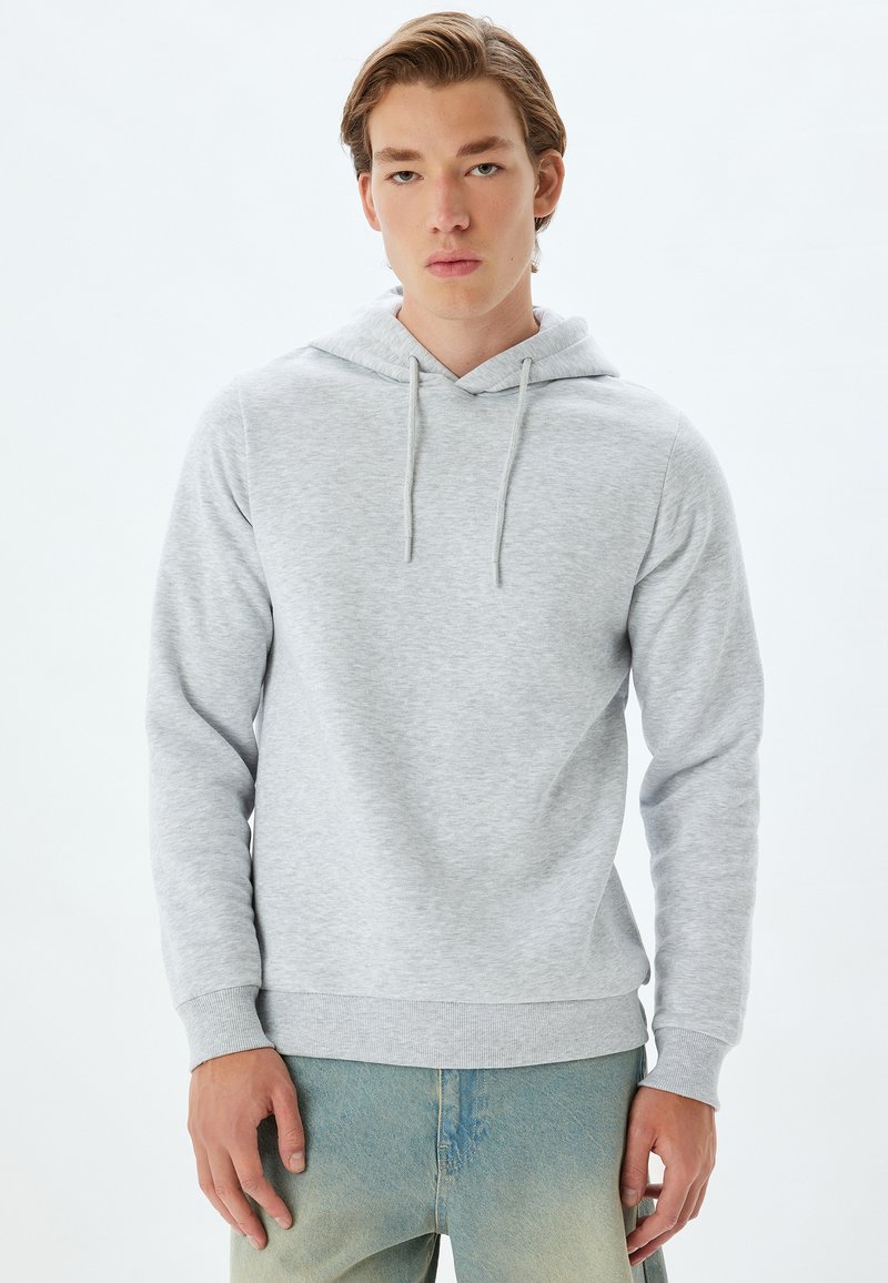 Grauer Kapuzenpullover aus weichem Stoff, mit einer vorderen Kängurutasche, Kordelzugkapuze und gerippten Bündchen. Kombiniert mit ausgewaschenen blauen Jeans.