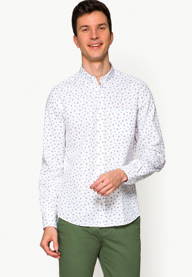 Biała koszula z długim rękawem i niebieskimi kwiatowymi wzorami, z klasycznym kołnierzykiem, w zestawie z zielonymi spodniami.