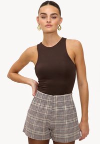 Body marron sans manches associé à un short taille haute à carreaux beige, marron et verts. Boucles d'oreilles créoles dorées en accents.