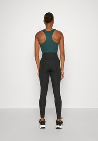 Rebrasta bezrukavna teal crop majica u kombinaciji s hlačama visokog struka crne boje, oboje napravljeno od rastezljivog materijala. Crno-bijele atletične tenisice.