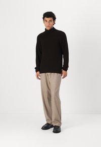 Donkerbruine geribbelde turtleneck trui, gecombineerd met lichtbruine wijde broek en zwarte instapschoenen. Eenvoudig, textuurontwerp.
