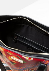 Sac à main noir avec un extérieur à motif floral, fermeture éclair, et un intérieur doublé de tissu comprenant une petite poche zippée et une texture lisse.