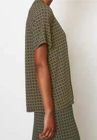 Top de manga corta en tejido verde con un patrón geométrico. Escote redondo y corte holgado. Textura suave. Combinado con una falda a juego con el mismo patrón.
