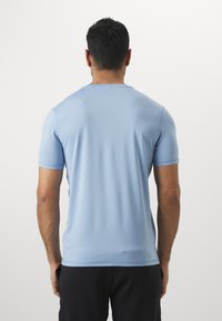 Camiseta de manga corta azul claro, fabricada con un tejido suave. Presenta un escote redondo y un dobladillo recto. La vista trasera muestra costuras mínimas y detalles de diseño.