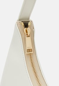 Borsa in pelle bianca con dettagli della cerniera dorata e rivestimento in canvas beige, caratterizzata da una texture liscia e una forma curva.