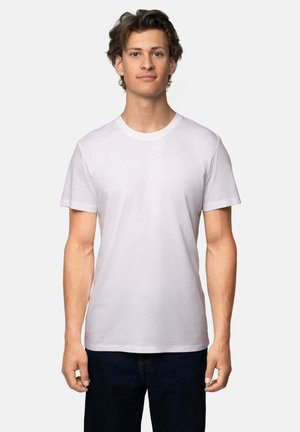 Hvid bomulds-T-shirt med rund hals og korte ærmer, tætsiddende pasform, vist på en person mod en neutral baggrund.