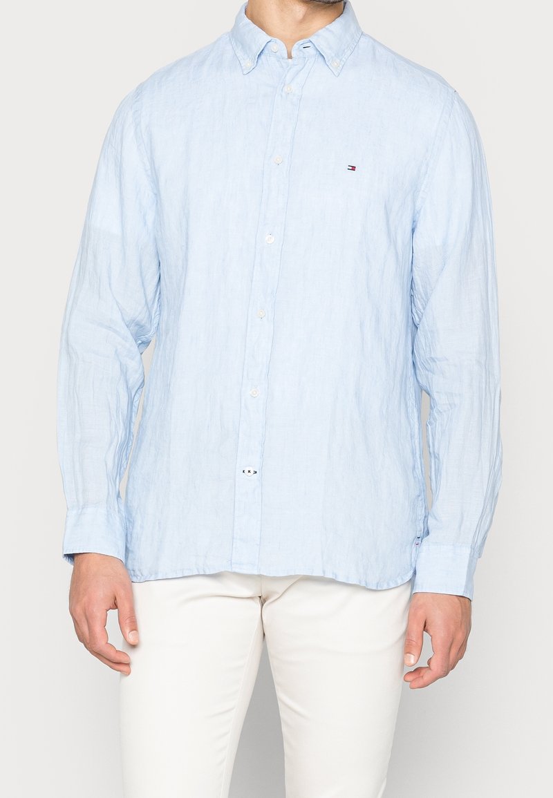Světle modrá lněná košile s dlouhými rukávy, s límečkem na button-down, předními knoflíky a malým logem na hrudi. Hladká textura.