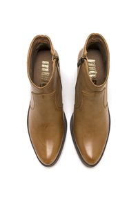 Un par de botas de cuero color carne hasta el tobillo con cremalleras laterales, punteras puntiagudas y suelas negras, vistas desde arriba sobre un fondo blanco.