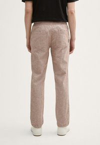 Lichtbruine, textuurpant met een elastische tailleband, twee achterzakken en een relaxte pasvorm, gecombineerd met witte sneakers.