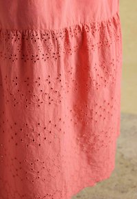 Rochie de bumbac corai, cu modele florale brodate și decupaje tip ochi de găină de-a lungul tivului. Textură moale cu detaliu design adunat.