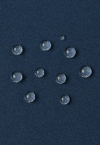 Gocce d'acqua che si accumulano su una superficie di tessuto testurizzato blu scuro, illustrando un materiale resistente all'acqua.