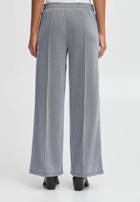 Pantalon gris clair à jambes larges avec un tissu texturé, une taille élastique et des coutures sur les côtés. Présente une coupe décontractée et arrive jusqu'aux chevilles.
