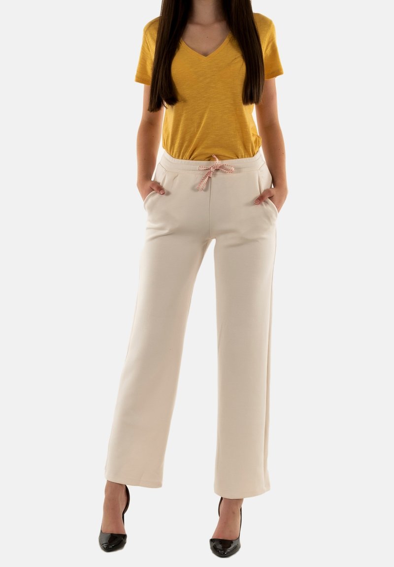 Pantalones de pierna ancha de color crema con una textura suave, cinturilla elástica, cordón rosa y bolsillos laterales, combinados con una camiseta amarilla de escote en v.